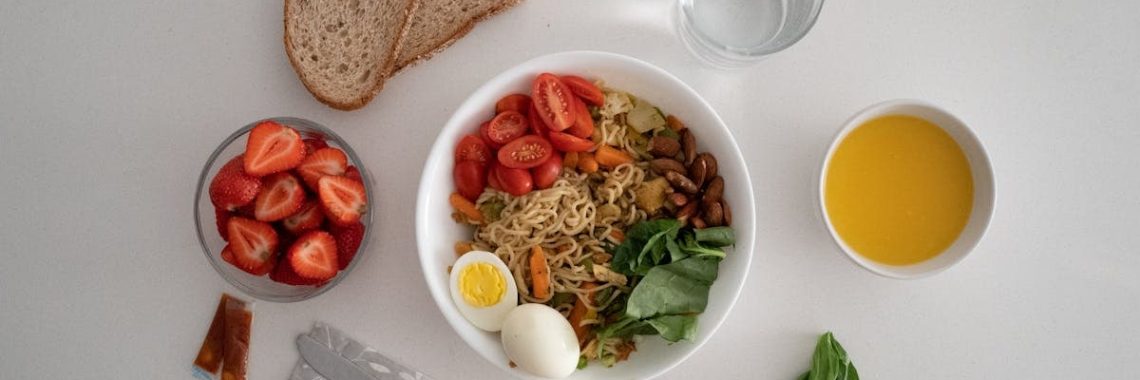 A balanced meal featuring a variety of healthy ingredients including noodles, eggs, almonds, strawberries, and fresh vegetables.